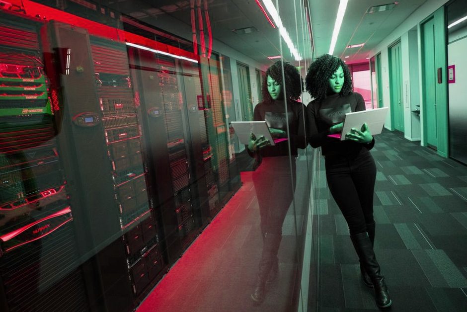 Femme sur un ordinateur portable dans un datacenter aux serveurs en miroir.